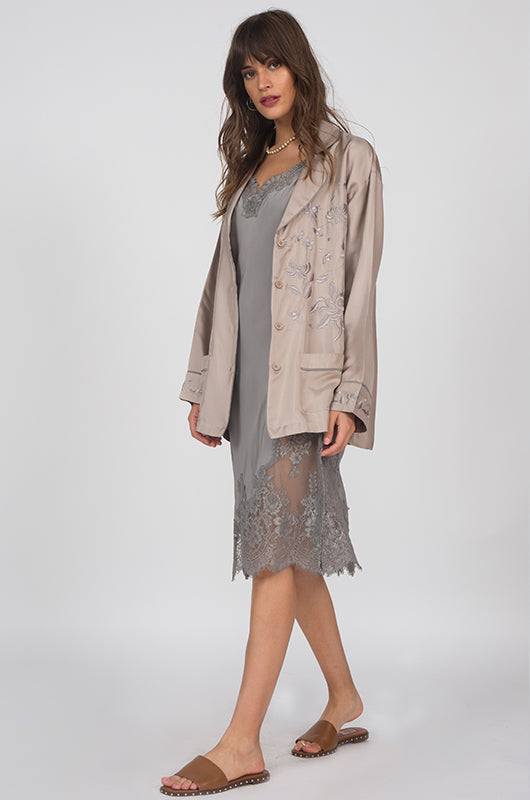 Model is wearing the Grace Lace Silk Dress in steeple grey with the Silk Pajama Shirt in camel on top, opened. Also worn with brown, flat, open toe, slip-in sandals.