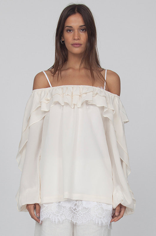 Model is wearing the Double Ruffle Silk Top in off white with the Coco Lace Silk Straight Cami in white peeking out from the hem of the ruffle top. Also worn with the Wide Leg Linen Belted Pants in dove.