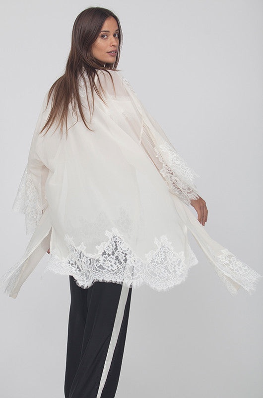 Model is wearing the Coco Lace Silk Kimono in off white, opened, with the Gigi Lace Silk Cami in white underneath with wide leg pants that are black with vertical white stripes on the sides.