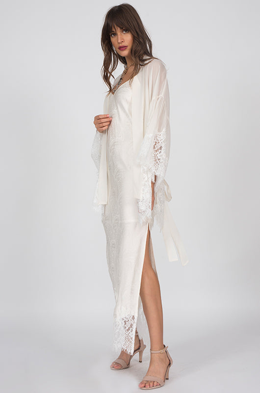 Side View to show slit; Model is wearing the Emma Silk Jacquard Slip Dress in dove with the Coco Silk Lace Kimono in dove. Also worn with open toe, ankle strap, nude colored high heels.