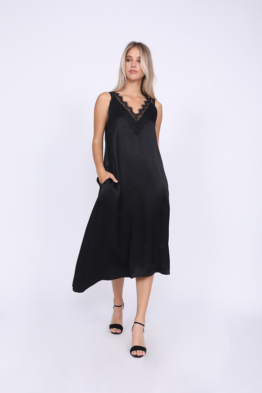Model is wearing the Hayley Asymmetric Dress in black with open toe, ankle strap, black high heels.
