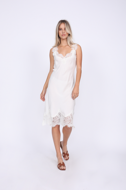 Model is wearing the Megan Coco Dress in white with brown, slip in, flat, open toe sandals.